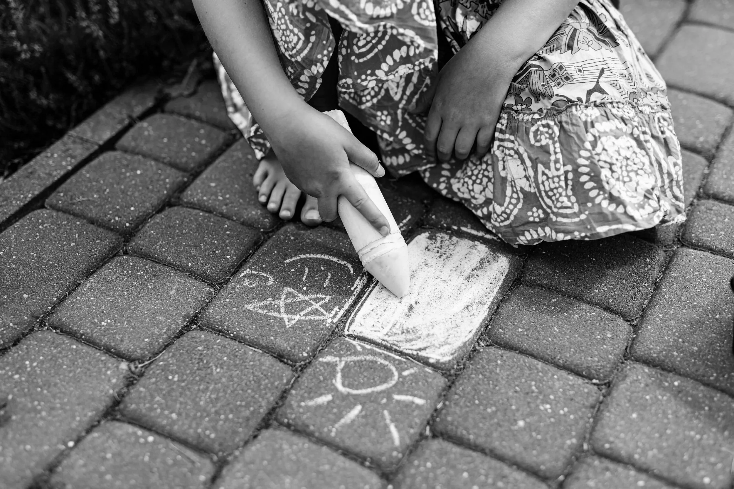 Child drawing with chalk on sidewalk, black and white photo.